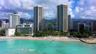 A drone shot of buildings and skyscrapers on a beautiful beach with crystal water under cloudy sky in Waikiki, Hawaii