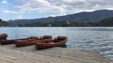 Yoğun ormanın arka planında, Bled Gölü kıyısındaki rıhtımlı teknelerin görüntüsü