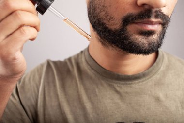 Minoxidil dolu bir damlayı tutan adamın yakın plan görüntüsü beyaz arka planda izole edilmiş sakal uzaması için başvuracak..