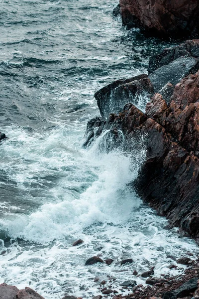 A vertical shot of splashing foamy waves on a cliff