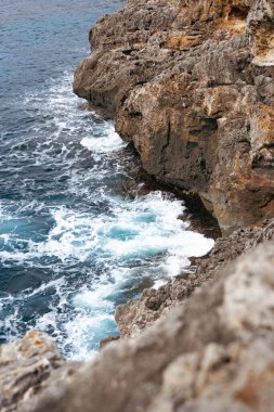 Arka planda kayalıklar olan dalgalı bir deniz görüntüsü.