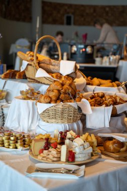 Tabakları peynir ve kruvasan dolu bir restoran masasının dikey görüntüsü.