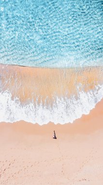 Deniz dalgaları sahili yıkarken güneşlenen bir kadının havadan görünüşü.