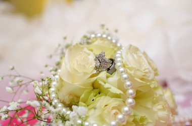 Lüks elmas yüzükler ve beyaz güllerin üzerinde inci bir kolye.