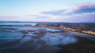 Gün batımında bulutlu bir gökyüzünün altındaki kumsal manzarası.