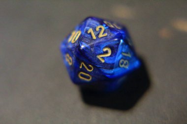 Üzerinde altın numaralar olan mavi metal bir D20 zar.