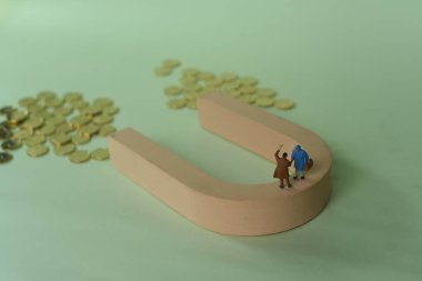 Altın sikkelerle bir mıknatısın dikey görüntüsü ve anlaşma yapan iki adamın heykeli.