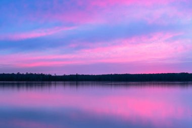 Gölün güzel manzarası ve kıyılarındaki ağaçlar alacakaranlık gökyüzüne karşı gün batımında suda görünür yansımalarla.