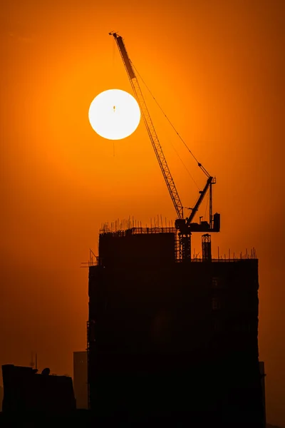 Arkasında Turuncu Güneş Olan Bir Binanın Üzerindeki Vinç Silueti — Stok fotoğraf