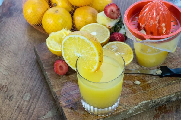 顶部的新鲜橙汁在圆形的玻璃与手动果汁机和成熟的水果在木板上 — 图库照片