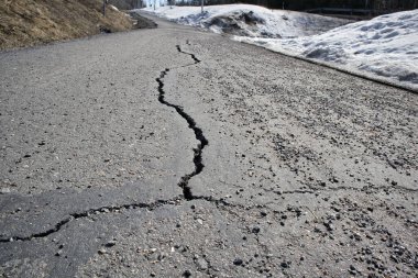 Güneşli bir günde asfalt bir yol yüzeyi çatlamış.