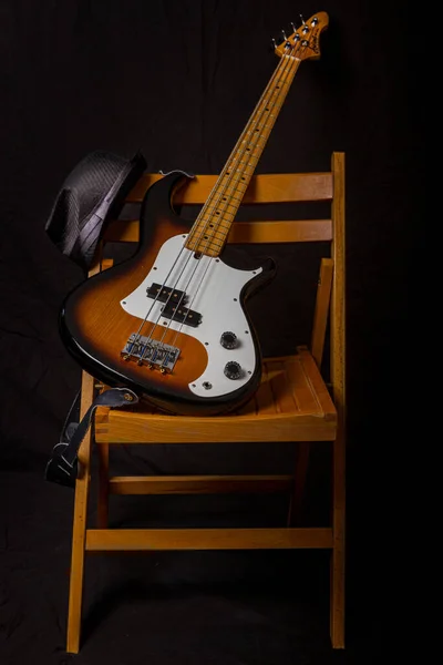 A vertical closeup of a bass guitar on a wooden chair against black background