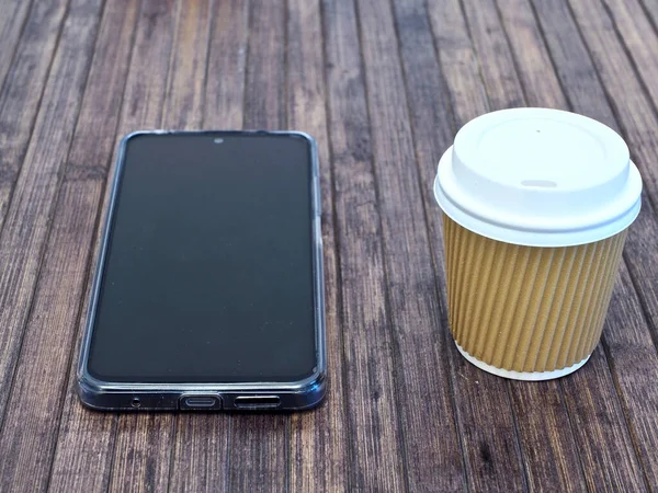 horizontal view of a take away coffee cup with a mobile phone on a wooden table
