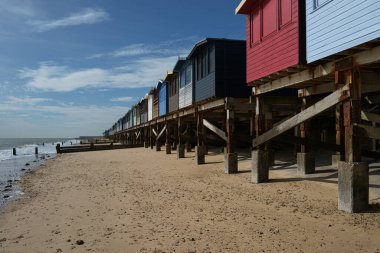 Kumlu bir sahilde, bulutlu bir gökyüzüne karşı renkli ahşap kulübeler.