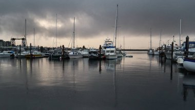 Gri bir yaz akşamı yağmuru bir eğlence sanatları limanında ve okyanus suyundaki teknelerin yansımaları..