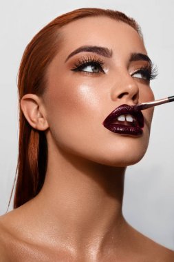 Beyaz bir arka plana ruj süren çekici bir kadının portresi.
