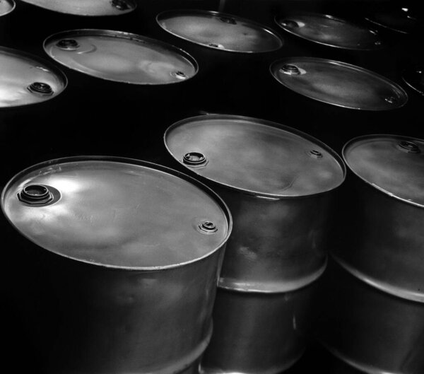 A grayscale shot of many gritty metal oil barrels
