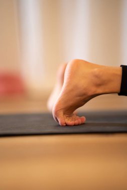 Matta üzerinde yoga yapan insan bacaklarının dikey görüntüsü.