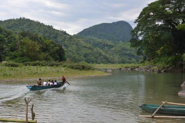 Birkaç kişinin mavi bir tekneyle Wawa Nehri, Rizal, Filipinler 'e gidişinin manzaralı bir görüntüsü.