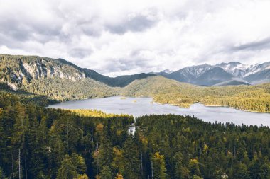 Eibsee Gölü 'nün güzel manzarası Almanya' da bulutlu gökyüzünün altında ağaçlar ve dağlarla çevrilidir.