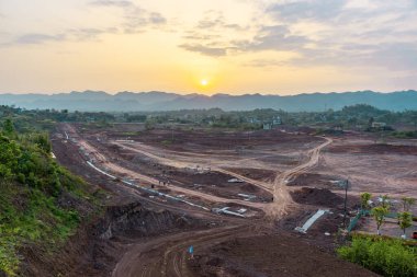 Büyük toprak tarlaları ve yeşil ağaçlarla dolu güzel bir manzara, sarı günbatımı gökyüzüne karşı evler.