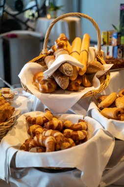 Tabaklar, sepetler dolusu ekmek çubukları ve kruvasanlarla dolu bir restoran masasının dikey yakın çekimi.