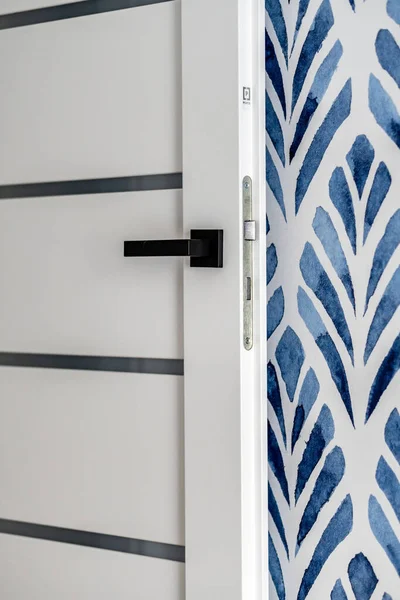 A vertical shot of an open white Porta brand door against a wall with a blue pattern