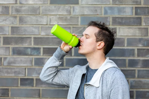 A young Caucasian male drinking water and taking a break after the jogging in nature