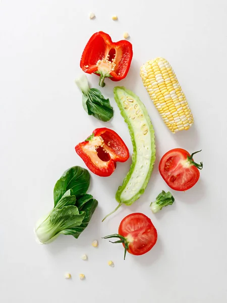 A top view of cut tomato, pepper, bitter gourd, corn and lettuce on white background