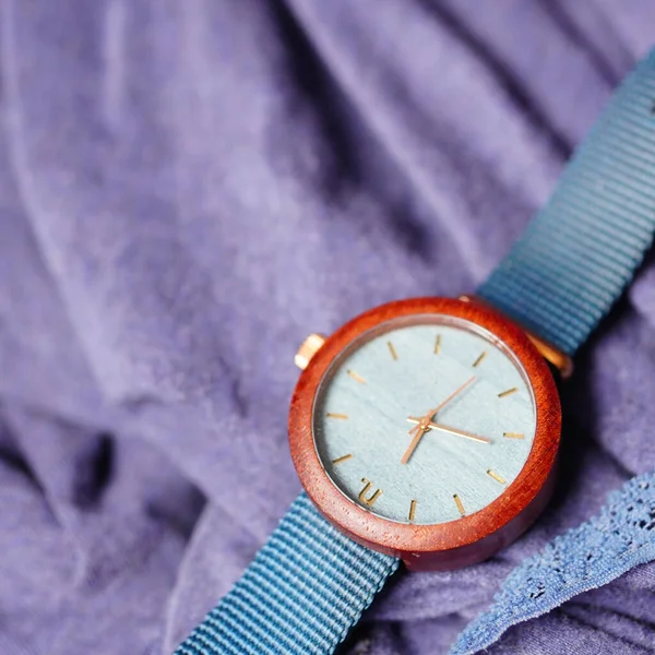 A closeup of a wooden woman watch with blue straps on purple fabric