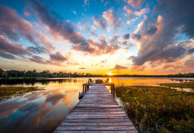 Florida 'da günbatımının dramatik arka planında gölde uzun bir ahşap iskele.