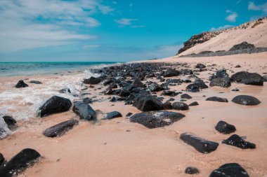 Kumsaldaki küçük siyah kayalara yakın çekim..