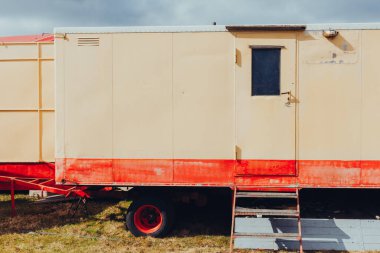 Çimlerin üzerine park etmiş kapısı ve merdiveni olan eski bir metal römork.