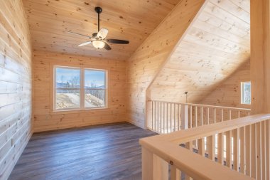 Ahşap tavanı, pencereleri ve merdivenleri olan boş bir salonun içi.