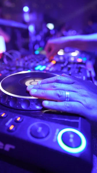 A vertical closeup of a DJ\'s hand controlling the music on the set at a party in the disco