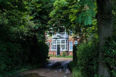 Yeşil ağaçların ve çalıların arkasındaki kırmızı tuğla bina..