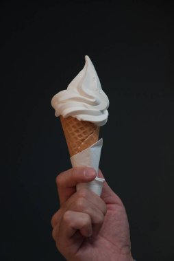 Dondurma külahını siyah arka planda tutan bir elin dikey yakın çekimi.