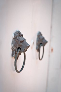 Beyaz bir duvarda iki aslanın baş kapı tokmağı dikey bir çekim