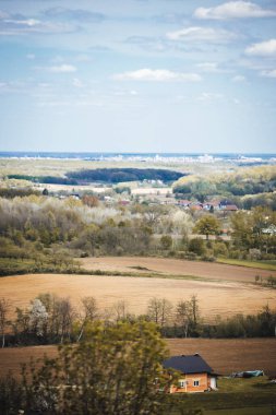 Kırsal kesimde bulutlu bir gökyüzünün altında yeşilliklerle çevrili bir kasabanın dikey görüntüsü.
