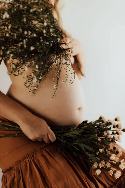 Kahverengi Etekli Hamile Bir Kadının Elinde Çiçeklerle Dikey Bir Fotoğrafı — Stok fotoğraf