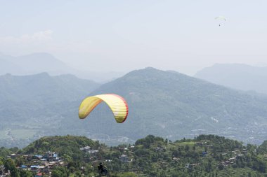 Nepal 'deki Sarangkot' tan Pokhara 'ya altında yemyeşil dağlar bulunan yamaç paraşütçülerinin hava görüntüsü.