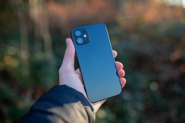 Bokeh arka planında iki kamera lensi olan akıllı telefonu tutan bir el.