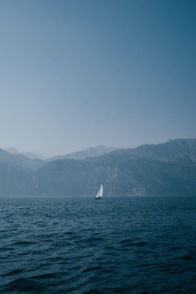A vertical distant view of a sailboat in the ocean with mountains in the background in Johannesburg, South Africa