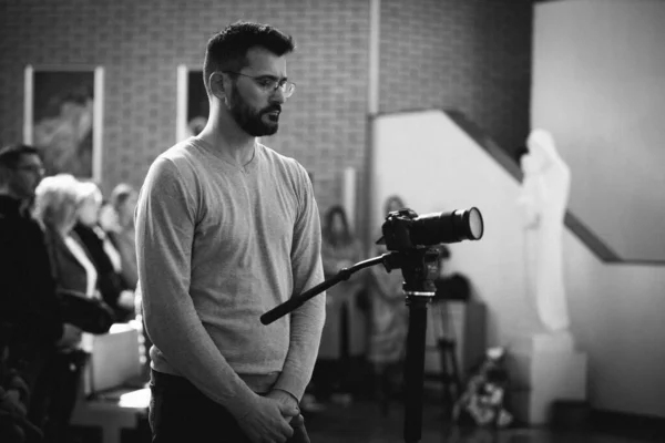 A black and white shot of an attractive male cinematographer at job with Sony camera on monopod