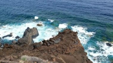 Engebeli bir volkanik kıyı manzarası ve kayaların üzerinde dalgaların kırıldığı bir okyanus. El Hierro, Kanarya Adaları 'nın kayalık sahili..