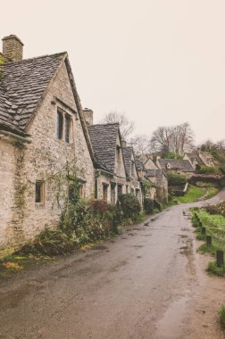 Bibury, Gloucestershire 'daki tarihi Cotswold kulübeleriyle aynı hizada bir yolun dikey çekimi.