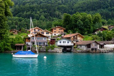 The sailboat on Lake Brienz against cottages surrounded by green vegetation. Interlaken, Switzerland. clipart