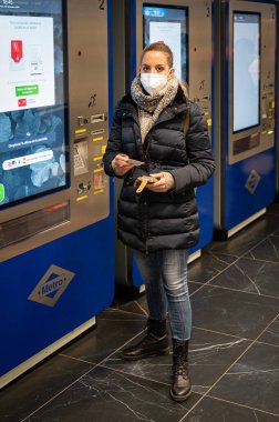 Maskeli genç kız, makineden metro bileti alıyor.