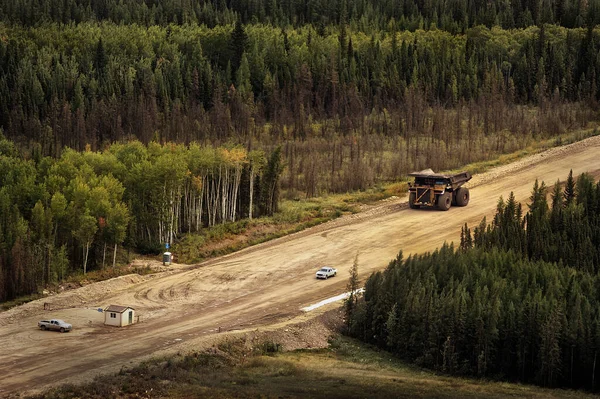背の高い緑の木々に囲まれた道路を走行する巨大なオイルサンド採掘トラック — ストック写真