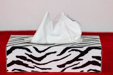 Kırmızı bir yüzey üzerinde beyaz kağıt mendillerle dolu bir zebra kutusunun yakın çekimi.